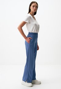Jasnoniebieskie spodnie z elastycznym paskiem w talii, z bocznymi kieszeniami, o prostym kroju z delikatnymi rozcięciami po bokach. Połączone z białą koszulką z dekoltem w kształcie litery V.