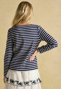 Langarmshirt mit navyblauen und weißen Streifen, weitem Ausschnitt, weichem Stoff und lockerer Passform, kombiniert mit einem cremefarbenen Rock mit Blumenstickerei.