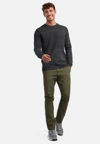 Dunkelgrauer strukturierter Pullover mit Rundhalsausschnitt, kombiniert mit olivgrünen Slim-Fit-Hosen und grauen Sportschuhen. Einfaches, modernes Outfit.