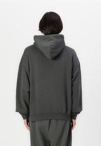 Sweat à capuche gris foncé, coupe oversize, mélange de coton doux, poignets et ourlet côtelés, texture lisse, design uni sans motifs.