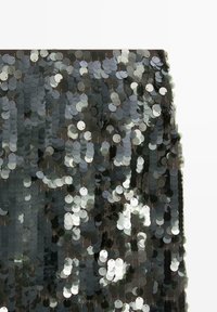 Black fabric covered with densely packed shiny black and silver sequins reflecting light with a shimmering effect.