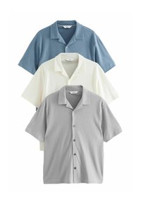 Tres camisas de manga corta: una azul claro con un patrón de diamantes, una blanca con un patrón texturizado y una gris con un diseño similar. Cada una tiene un collar.