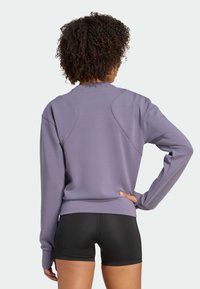 Felpa viola con maniche lunghe e scollatura rotonda, caratterizzata da una texture liscia e dettagli a pannello sulle spalle, abbinata a pantaloni corti neri.