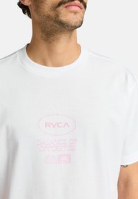 White cotton t-shirt featuring pink graphic text and logos on the front, round neckline, and short sleeves. Smooth texture.