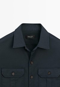 Mørkeblå skjorte med knapper foran, spids krave, to brystlommer med knapper og "Massimo Dutti" mærke indeni kraven.