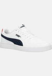 Sneaker bianco realizzato in materiale sintetico con superficie testurizzata. Presenta una striscia blu navy, stringhe e un piccolo accento rosso sul tallone.