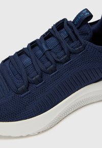 Navy blue sneaker with knit upper, textured accents, elastic laces, and a white midsole. Features a lightweight, breathable design.