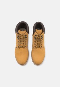 Bottes à chevilles en daim jaune avec un col rembourré marron foncé, œillets noirs et lacets dorés. Semelle en caoutchouc texturée pour une meilleure adhérence.