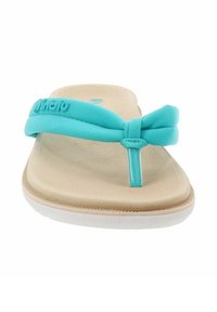 Un infradito turchese con una morbida cinghia e un fondo beige, con una suola bianca leggermente curvata e con una texture minimale.