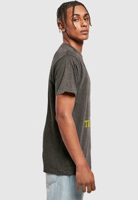 Grå bomulds T-shirt med korte ærmer, rund hals og et trykt grafisk motiv i gul med tekst. Pasformen er afslappet og casual.