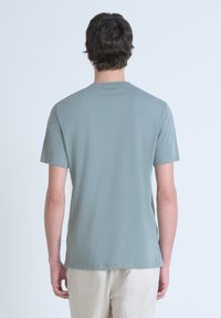 Camiseta de algodón verde claro con mangas cortas, cuello redondo y un corte holgado. Textura suave con un mínimo de marca en la parte posterior.