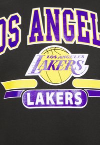 T-shirt noir avec un texte audacieux en blanc et violet : « LOS ANGELES LAKERS », accompagné d'un graphisme de ballon de basket jaune et d'accents courbés jaunes.