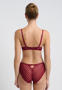 Set di lingerie bordeaux composto da un reggiseno in pizzo con spalline regolabili e culotte a vita alta coordinate, che mostrano motivi a zigzag e un dettaglio a fessura.