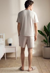 Light beige striped short-sleeve t-shirt and matching shorts, made of soft fabric. Features a relaxed fit and back pockets, paired with slippers.