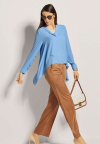 Himmelbluse mit langen Ärmeln und V-Ausschnitt, kombiniert mit beigen Palazzo-Hosen und einer cremefarbenen Handtasche mit braunen Akzenten. Beigefarbene High Heels.