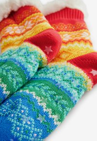 Strickhandschuhe in mehrfarbigen Mustern: rot, gelb, grün und blau mit Sternakzenten. Der weiche Bund mit weißem Fellbesatz rundet das Design ab.