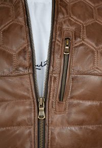 Bruine leren jas met een hexagonaal patroon, dubbele ritsen en een witte voering met zwarte stiksels.