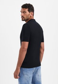 Zwarte polo met korte mouwen, gemaakt van een gladde stof. Draagt bij lichte blauwe denim jeans, die een ontspannen pasvorm en casual stijl laten zien.