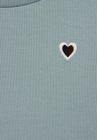 Tissu côtelé bleu clair avec un petit motif de cœur brodé, comportant des sections beige, marron foncé et marine sur le cœur.