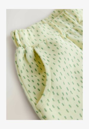 Világossárga anyag kis zöld pöttyös mintával, rugalmas derékpánttal és oldalsó zsebekkel. Puha tapintású, laza kialakítás.