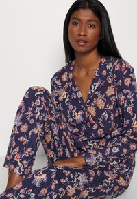 Marinblå blommig pyjamasuppsättning med färgglada mönster. Har lång ärm, knappstängning framtill och slim-fit byxor med ett tryck i hela. 