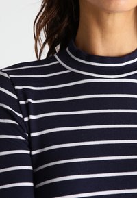 Granatowa bluzka z długim rękawem w białe poziome paski, z wykończeniem w formie stójki oraz miękką, gładką teksturą materiału.