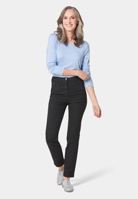 Un haut bleu clair à manches longues associé à un jean noir taille haute. La tenue présente une coupe slim avec des coutures discrètes et des chaussures grises.