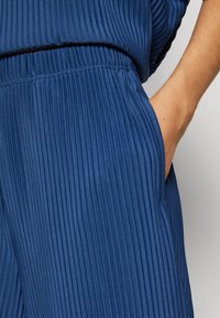 Main reposant dans la poche d'un pantalon bleu en tissu côtelé avec ceinture élastique et haut côtelé assorti.