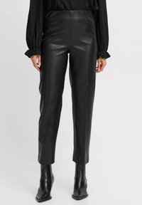 Pantaloni in pelle nera con una vestibilità slim, caratterizzati da una texture liscia e una vita alta. Abbinati a stivali neri alla caviglia a punta.