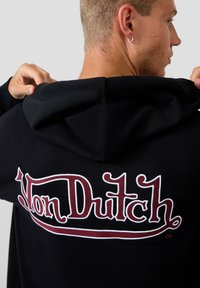 Schwarzer Hoodie mit einem großen gestickten "Von Dutch"-Logo in Weiß und Bordeaux, mit Kapuze und weichem Material.