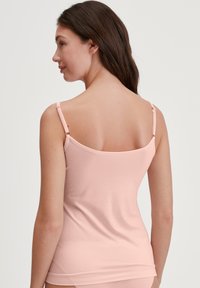Light pink tank top with thin straps, made of soft, stretchy fabric. Features a scoop back and a smooth texture.