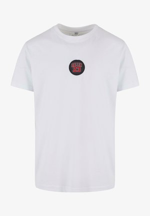 T-shirt bianco in cotone con un patch nero rotondo sul petto con "BALLIN 23" in lettere rosse e nere. Maniche corte, design a collo rotondo.