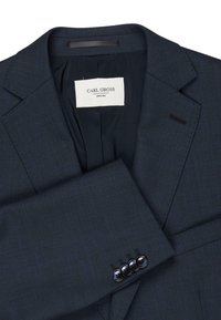 Navyblauwe blazer van gestructureerde stof, met een notch lapel, drie zwarte knopen op de manchetten en een label met de tekst "CARL GROSS."
