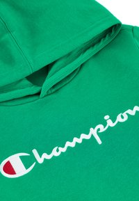 Felpa verde in cotone con tasca frontale, cappuccio con cordino e logo "Champion" ricamato in bianco con accenti rossi e bianchi.