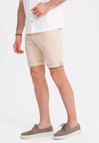 Shorts beiges à revers, réalisés en matériau doux. Assortis à des chaussures en daim grises avec des semelles blanches.