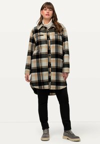 Karierte Jacke in Beigetönen, Schwarz und Orange. Mit Knopfleiste vorne, zwei Brusttaschen und einem leicht längeren Rückenbaum.