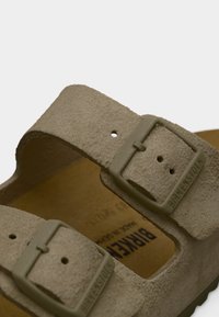 Κοντινό πλάνο από τα μπεζ λουριά ενός σανδαλιού Birkenstock με ρυθμιζόμενες αγκράφες και μαλακή σουέτ υφή.