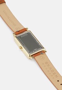 Zlaté obdélníkové hodinky s černým nerezovým ciferníkem, pravý hnědý kožený pásek s ražbou "Skagen Denmark."