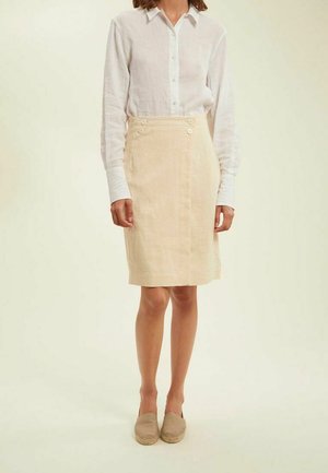 Jupe en lin de couleur beige clair, longueur genou, avec des boutons sur le devant et un design ajusté. Associée à une chemise blanche à boutons et à des espadrilles beiges.