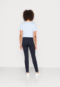 Camiseta corta azul claro, de mangas cortas, combinada con pantalones ajustados azul marino; textura suave, diseño sencillo, llevada con zapatillas blancas.