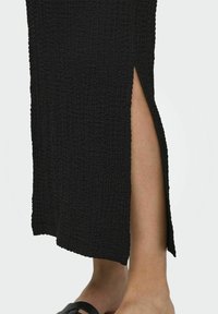 Falda midi negra hecha de una tela texturizada con una abertura lateral. Presenta una superficie arrugada y un diseño simple de corte recto.