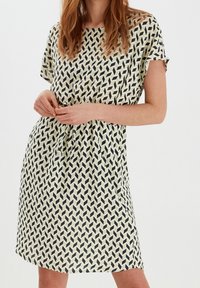 Kurzärmeliges Kleid aus hellgrünem Stoff mit einem schwarzen geometrischen Muster, das einen entspannten Schnitt und einen verstellbaren Kordelzug in der Taille bietet.