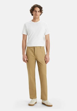 Beige cotton pants with a straight-leg fit, paired with a plain white crew-neck t-shirt and white sneakers with tan accents.