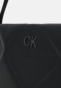 Borsa in pelle nera con un design trapuntato e logo "CK" impresso. Il materiale ha una texture liscia con una leggera lucentezza.