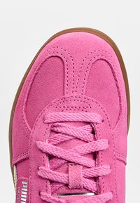 Baskets en daim rose vif avec de larges lacets roses, coutures détaillées et bord de semelle en caoutchouc marron, vue de dessus montrant la pointe et la zone des lacets.