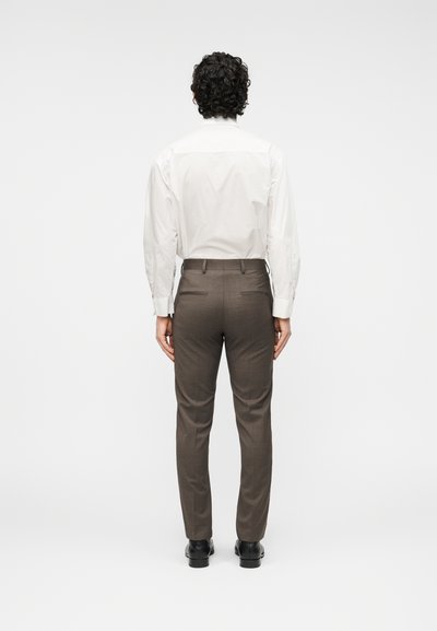 Λευκό πουκάμισο με κουμπιά και μακριά μανίκια, συνδυασμένο με καφέ παντελόνι ραμμένο καλαίσθητα. Η εμφάνιση έχει καθαρή, δομημένη όψη, παρουσιαζόμενη από πίσω.