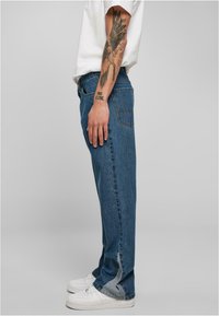 Blauwe denim jeans met een rechte pasvorm, vijf zakken en zichtbare stiksels; gedragen met witte sneakers en een aangesloten wit shirt.
