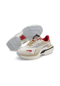 Puma Sneaker mit einem Obermaterial aus beigem Stoff, roten und blauen Akzenten, dicker weißer Sohle, strukturiertem Außensohle und khakifarbenen Details.