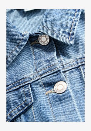 Giacca di jeans azzurro chiaro con collo a punta, due tasche anteriori, bottoni a pressione metallici e dettagli di cucitura a contrasto.