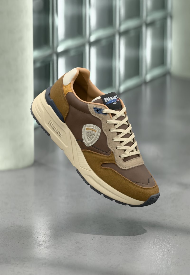 Scarpa sportiva marrone e beige con tomaia in suede e pelle, chiusura con lacci, suola in gomma e patch con logo laterale.